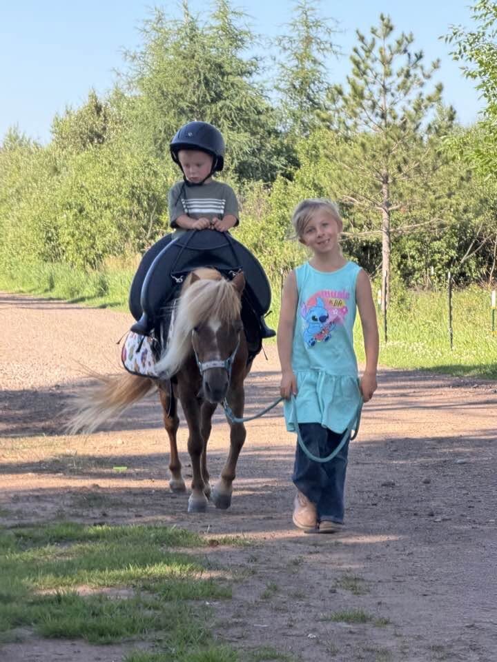 A young vaulter rides a pony led by a helper down a farm road at Full Circle Vaulting in Cloquet, Minnesota